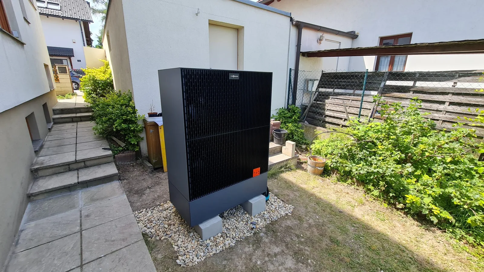 Neu aufgestellte Viessmann-Wärmepumpe auf einem Kiesbett im Garten eines Wohnhauses